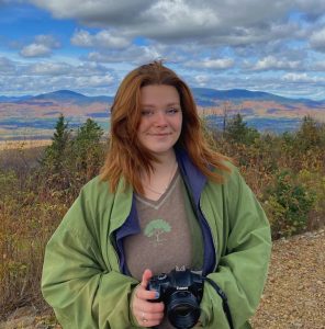 Young woman holding a camera with mountains in the background