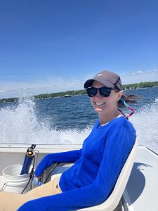 Meghan in a bright blue top sits at the stern of a boat with water splashing all around.