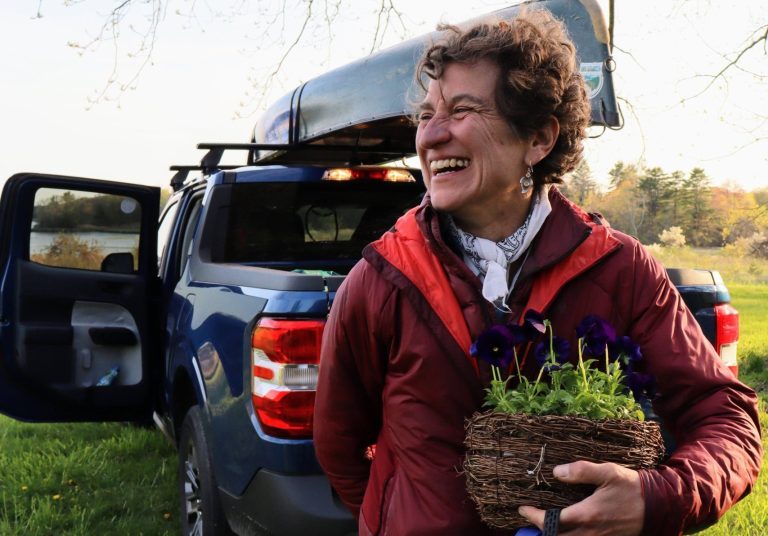 Jen holding a gift of flowers in front of her truck, loaded with her canoe