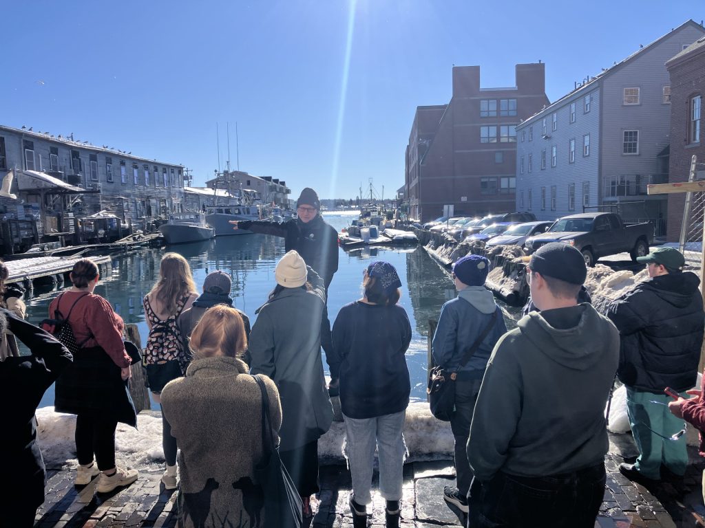 a group of students stand listening to Will give a tour of the harbor