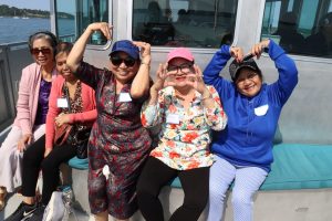 5 older women make heart shapes with their hands on a boat trip