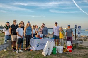 Clean-up volunteers stand with the bags of trash, water in the background