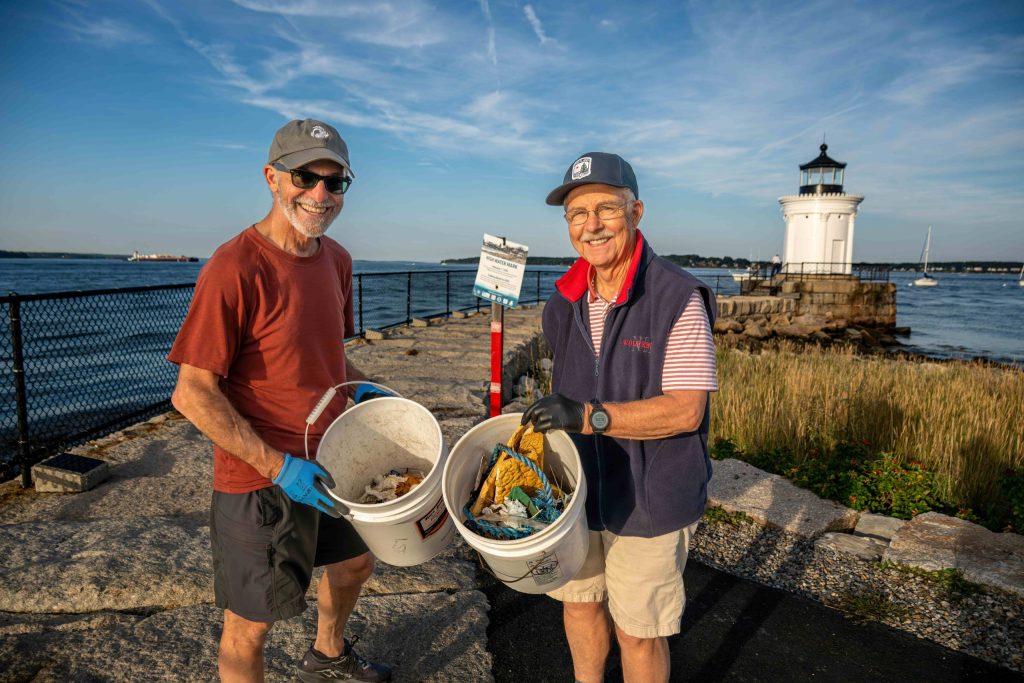 Two smiling volunteers hold up buckets of trash